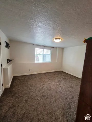 Room featuring textured ceilings, neutral wall tones, wall-to-wall carpeting, a single-pane window with a metal rod, and a flush-mount circular ceiling light