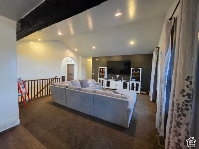 Vaulted ceiling featuring an exposed decorative timber beam, recessed lighting, accent wall, and a wood-slat balustrade