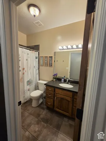 Bathroom featuring tile flooring, wood cabinetry with stone-finish countertop, undermount sink, and multi-bulb vanity lighting