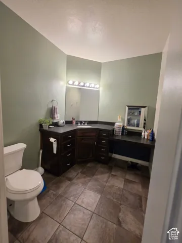 Dark wood cabinetry with stone-finish countertops, tile flooring, integrated vanity with recessed basin, and wall-mounted vanity lighting
