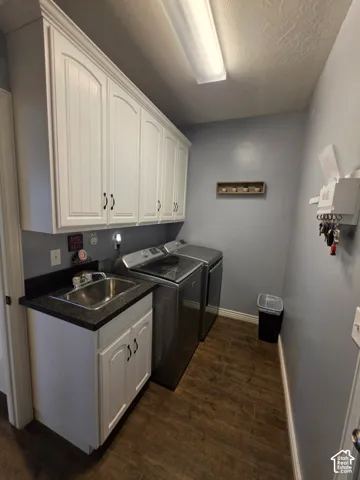 Laundry area featuring white shaker-style cabinetry, dark solid-surface countertops, an undermount stainless steel sink, and wood-finish flooring