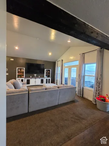 Vaulted ceilings featuring an exposed dark-stained timber beam, large windows with natural lighting, and built-in white cabinetry