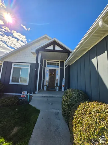 Exterior entrance featuring dark vertical siding, contrasting white shingle accents, a covered porch with a decorative timber truss, and a solid wood front door with glass inlay