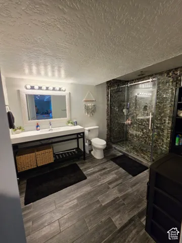 Bathroom featuring a walk-in shower with stone tile surround, sliding glass door, wall-mounted vanity with integrated basin, and wood-finish tile flooring