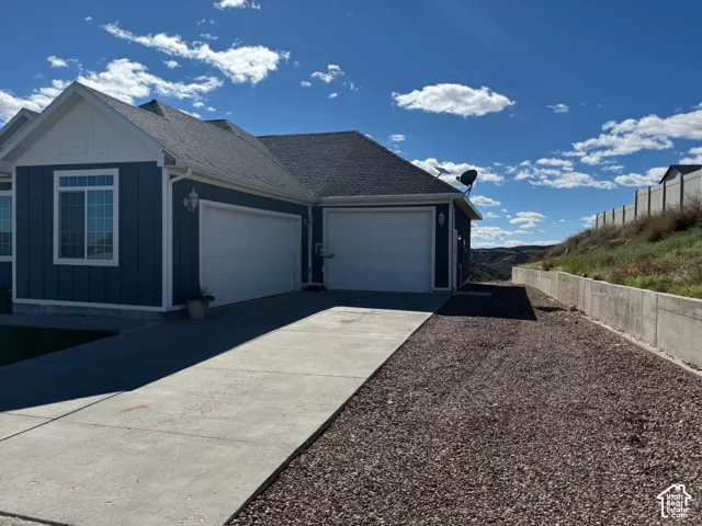 Blue siding exterior with white trim, asphalt shingle roof, two-car garage, concrete driveway, and concrete retaining wall