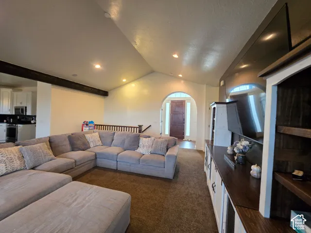 Vaulted ceilings featuring decorative dark wood-finish ceiling beams, recessed lighting, arched entryway, and built-in cabinetry with dark wood-finish shelving