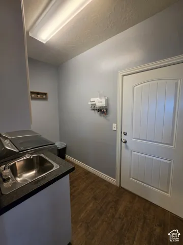 Utility space featuring wood-finish flooring, a stainless steel sink with a dark countertop, and a solid-core entry door