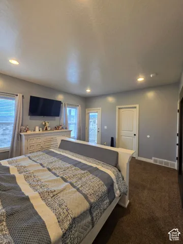 Spacious room featuring recessed lighting, carpeted flooring, neutral wall paint, two windows, and a glass-paneled exterior door