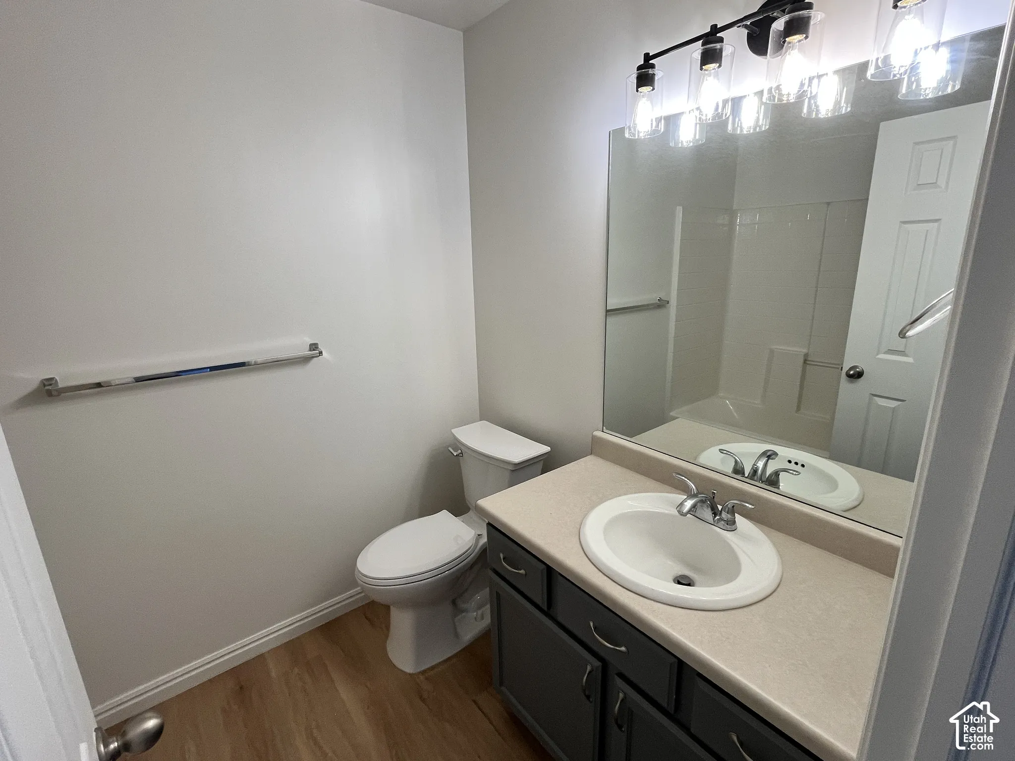 Bathroom featuring a vanity with dark cabinetry and a neutral countertop, undermount sink, multi-light fixture, and wood-finish flooring