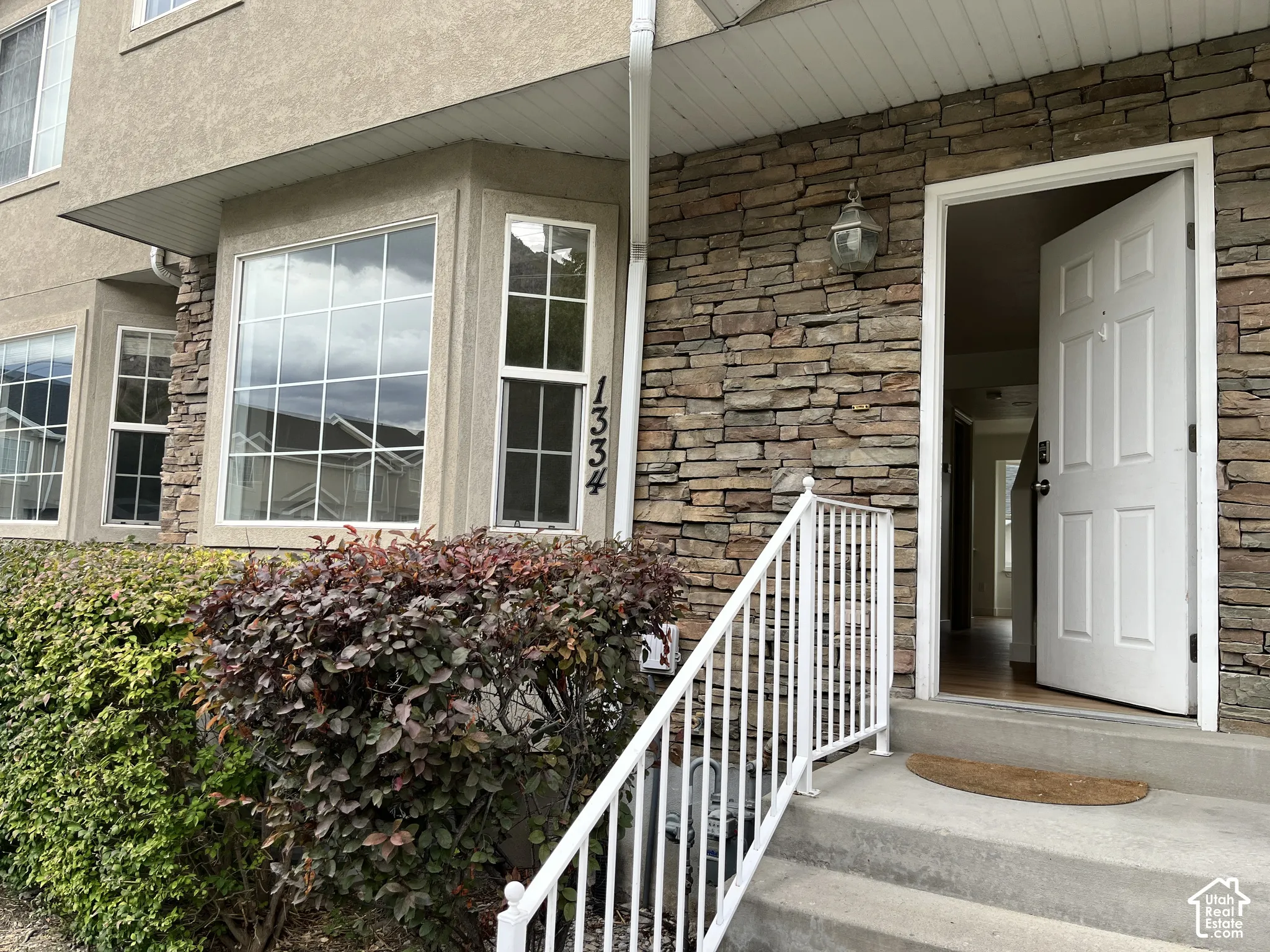 Exterior entrance featuring natural stone veneer siding, a bay window with a grid pattern, and a white metal railing leading to concrete steps