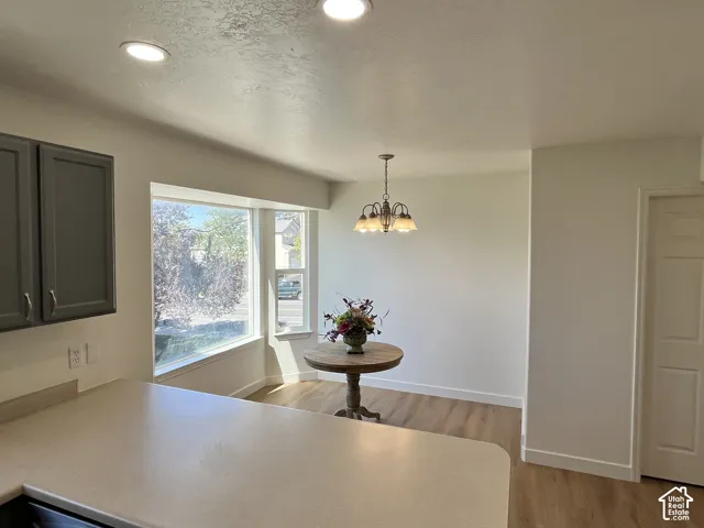 Kitchen area featuring wood-finish flooring, charcoal-toned cabinetry, recessed lighting, a multi-arm pendant light fixture, and a large bay window