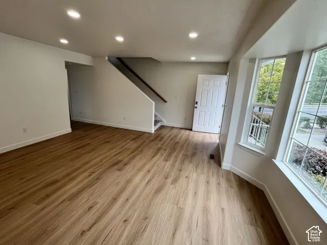 Open-concept interior featuring wood-finish flooring, recessed lighting, a bay window, and a staircase with a wooden handrail