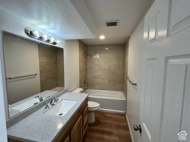 Bathroom featuring wood-finish flooring, vanity with a speckled countertop, integrated sink, and a tub-shower combination with full-height tile surround