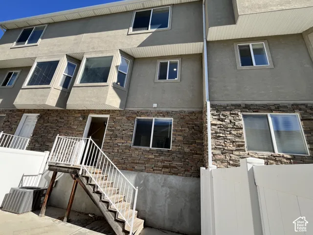 Multi-level exterior featuring stucco siding, stone veneer accents, bay windows, and an elevated wooden staircase with metal railings