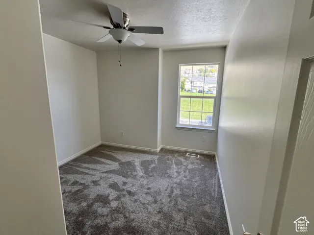 Neutral-toned interior room featuring wall-to-wall carpeting, a single-pane window, and a ceiling-mounted light fixture with an integrated fan