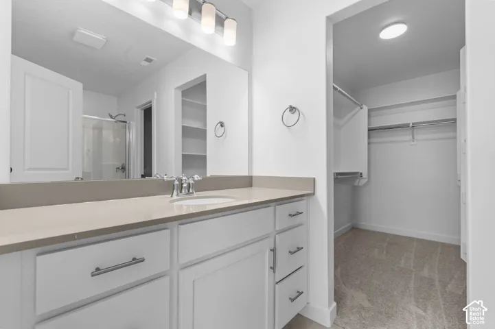 Bathroom featuring a white vanity with a composite countertop, an integrated sink, polished chrome fixtures, and an oversized mirror, paired with a walk-in closet containing built-in shelving