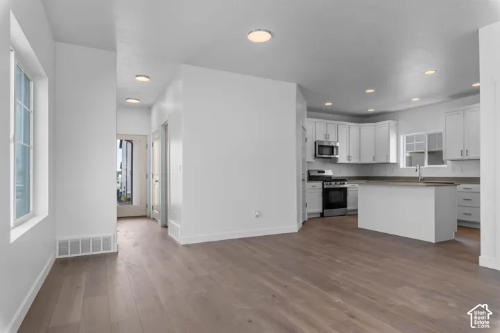 Kitchen featuring white shaker-style cabinetry, quartz countertops, a center island, stainless steel appliances, and wood-finish flooring