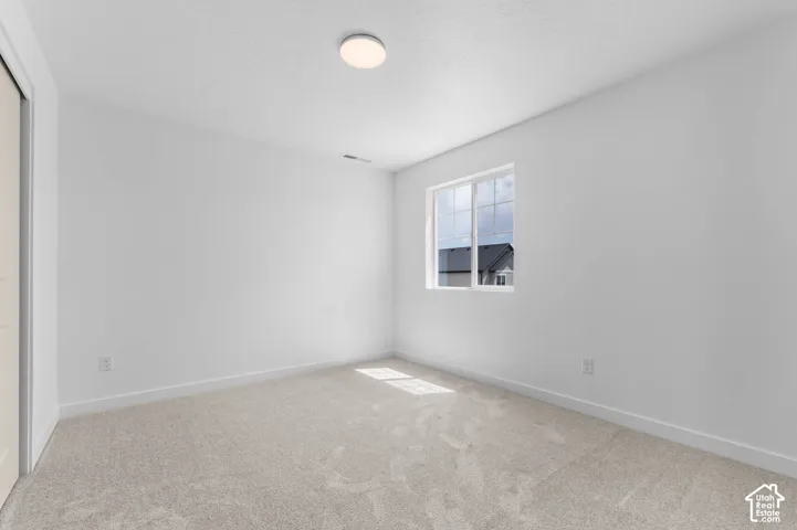 Neutral-toned carpeting, crisp white walls, single-pane sliding window, and a flush-mount circular ceiling light fixture