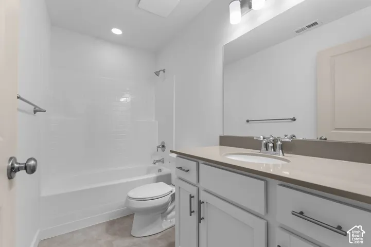 Bathroom featuring a vanity with neutral-toned stone-style countertop, undermount sink, white cabinetry with dark hardware, a large wall-mounted mirror, and a tub-shower combination with subway-style tile surround