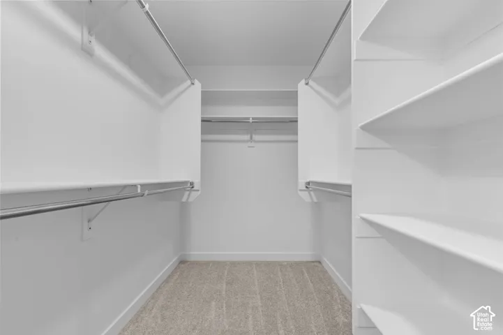 Walk-in closet featuring white built-in shelving, dual-level metal hanging rods, and neutral carpeting