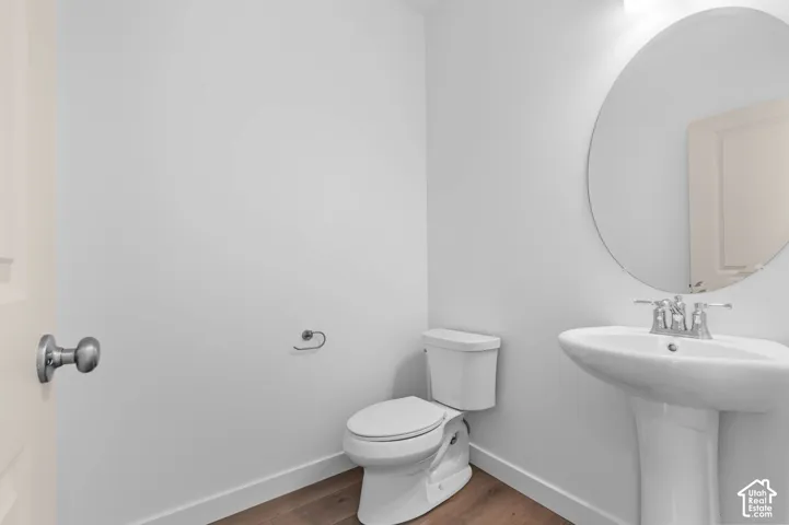 Powder room featuring wood-finish flooring, a white pedestal sink with chrome faucet, an oval frameless mirror, and a standard-height toilet