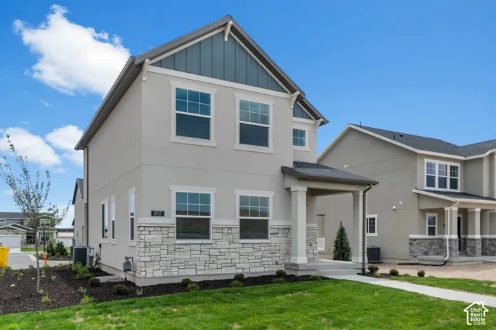 Two-story exterior featuring a light gray stucco finish, stone veneer accents, vertical siding gable detailing, and a covered front porch with square columns