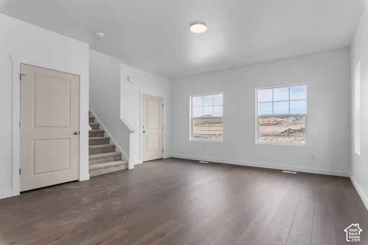 Interior space featuring wood-finish flooring, two multi-pane windows, neutral wall paint, and a carpeted staircase