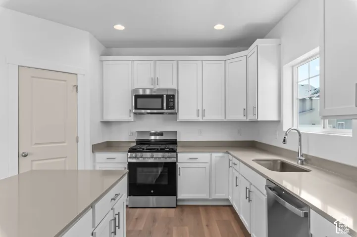 Kitchen featuring white shaker-style cabinetry, stainless steel appliances, neutral stone-finish countertops, and wood-finish flooring