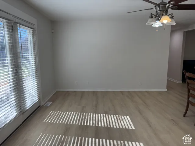 Wood-finish flooring, glass-paneled patio door with blinds, and ceiling fan with multi-bulb light fixture