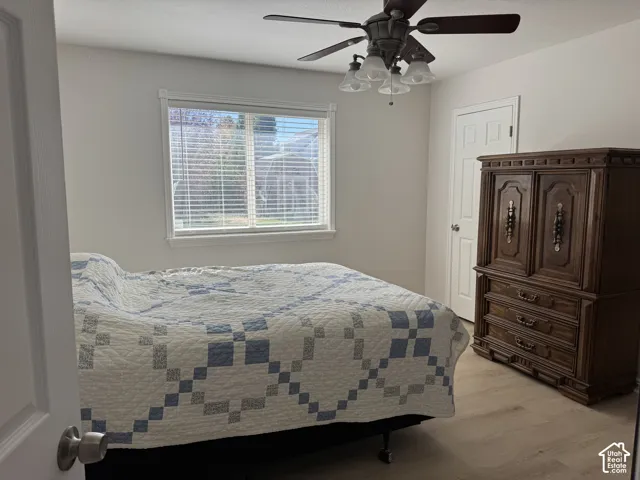 Neutral-toned room featuring wood-finish flooring, a multi-paneled door, and a ceiling fan with integrated glass-shade lighting