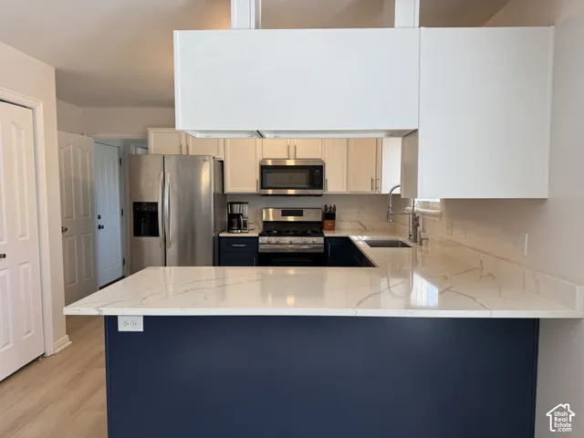 Kitchen featuring stone-finish countertops, stainless steel appliances, dual-tone cabinetry, and wood-finish flooring