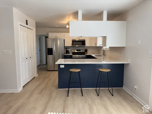 Kitchen featuring a peninsula with solid-surface counters, navy lower cabinetry, stainless steel appliances, and wood-finish flooring