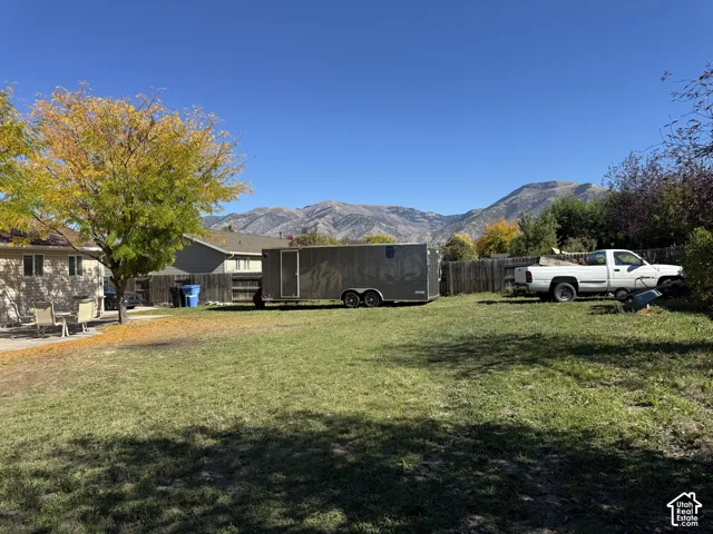 Expansive backyard featuring a concrete patio, wood fencing, mature trees, and a mountain backdrop