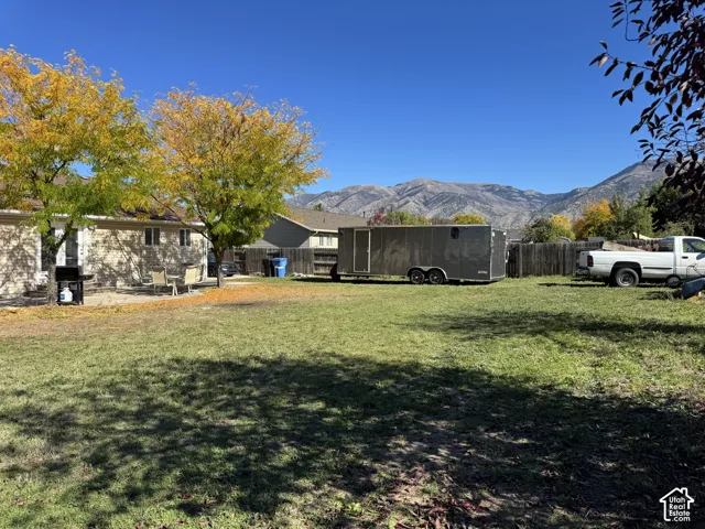 Expansive backyard featuring a concrete patio, mature trees, wood fencing, and a mountain backdrop
