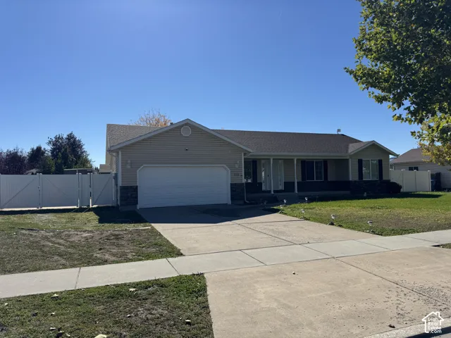 Single-story residence featuring horizontal siding, stone veneer accents, an attached two-car garage, and double white vinyl gate fencing