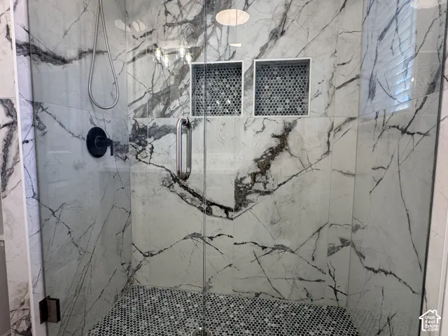 Walk-in shower featuring floor-to-ceiling large-format veined tile, integrated dual wall niches with mosaic tile accents, mosaic tile flooring, a frameless glass door, and matte black fixtures