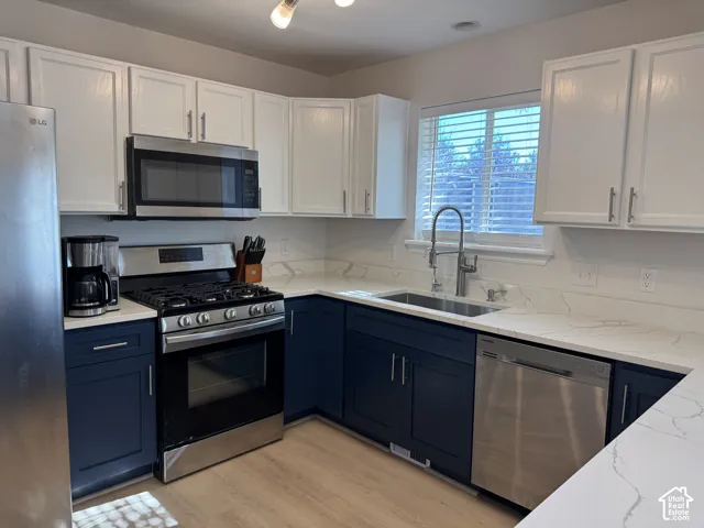 Kitchen featuring two-tone cabinetry, white countertops with veining, stainless steel appliances, wood-finish flooring, and a gooseneck faucet