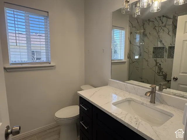 Bathroom featuring a dark wood vanity with a stone countertop, an integrated sink with a metal faucet, a glass-enclosed shower with tiled walls and built-in niches, and a large vanity mirror with multi-bulb light fixture