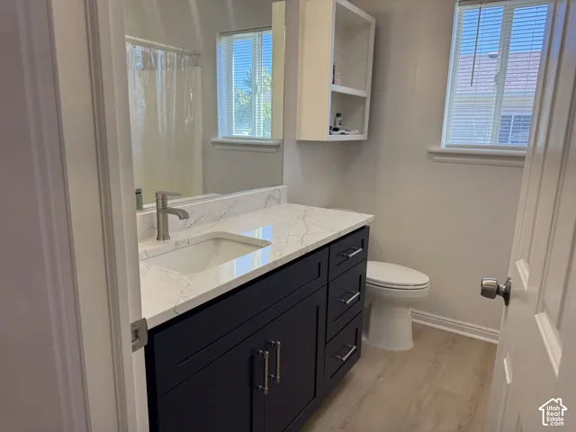 Bathroom featuring a dark-toned vanity with brushed metal hardware, a stone-patterned countertop with an integrated rectangular sink, a wall-mounted storage cabinet, and wood-finish flooring