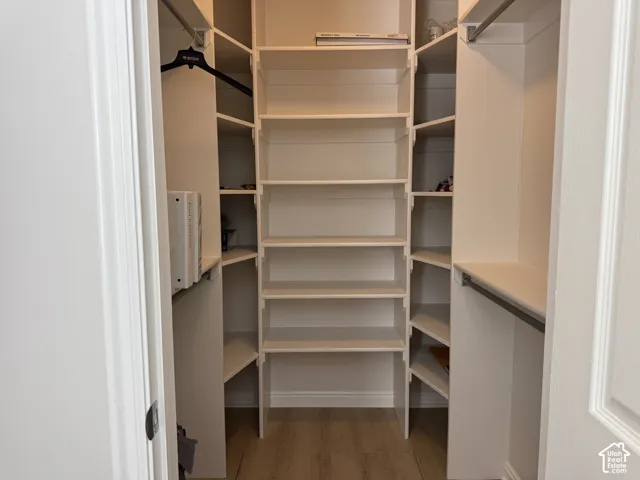 Built-in storage closet featuring custom white shelving, corner shelves, and metal clothing rods with wood-finish flooring