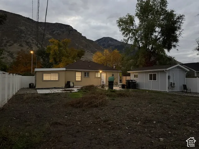Exterior lot featuring a mountain backdrop, a detached auxiliary structure, white vinyl perimeter fencing, and concrete patio areas