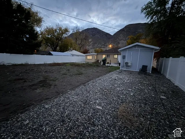 Backyard space featuring a white vinyl privacy fence, gravel surfacing, a detached storage structure, and a mountainous backdrop