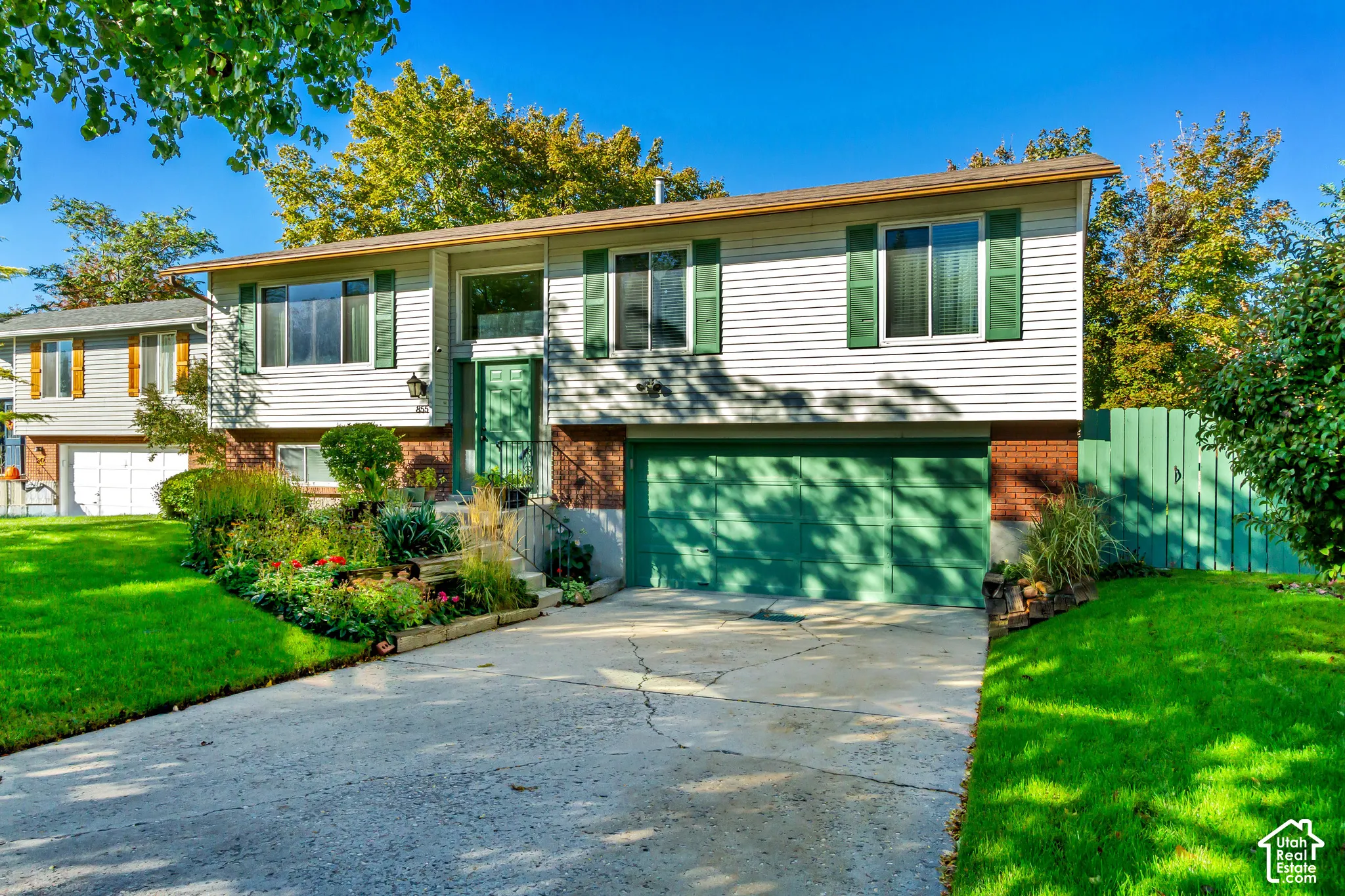 Split-level exterior featuring horizontal siding, a red brick base, an attached two-car garage, and landscaped garden beds