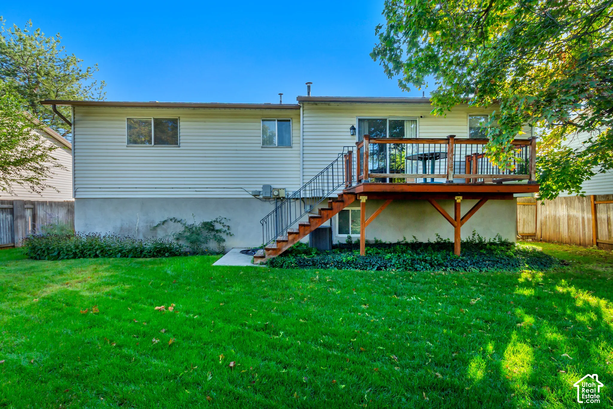 Rear exterior featuring horizontal vinyl siding, raised wood deck with balustrades, staircase with metal railings, and a concrete patio
