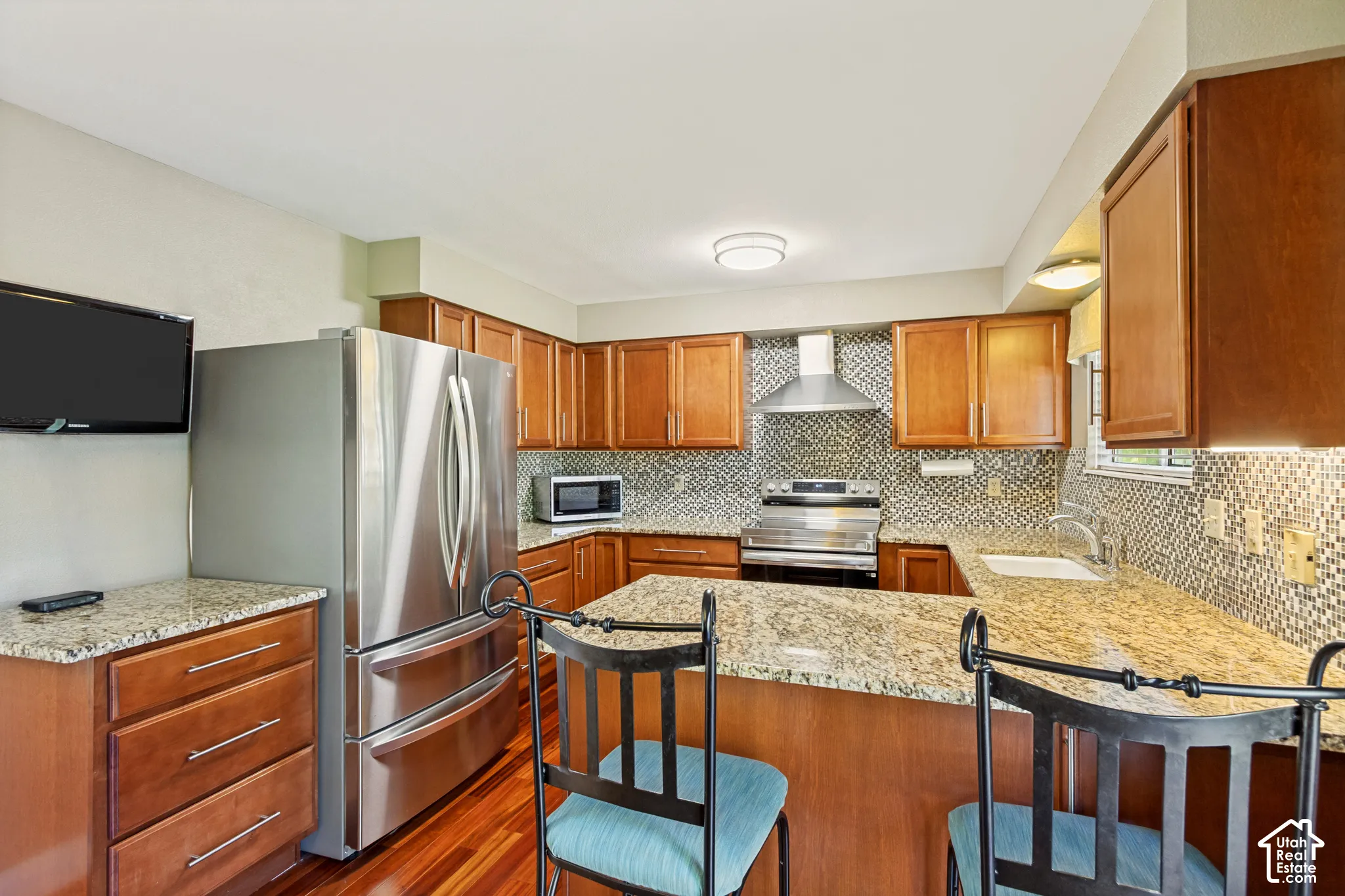 Kitchen featuring natural wood-finish cabinetry, stone-surface countertops, stainless steel appliances, patterned tile backsplash, and wood-finish flooring
