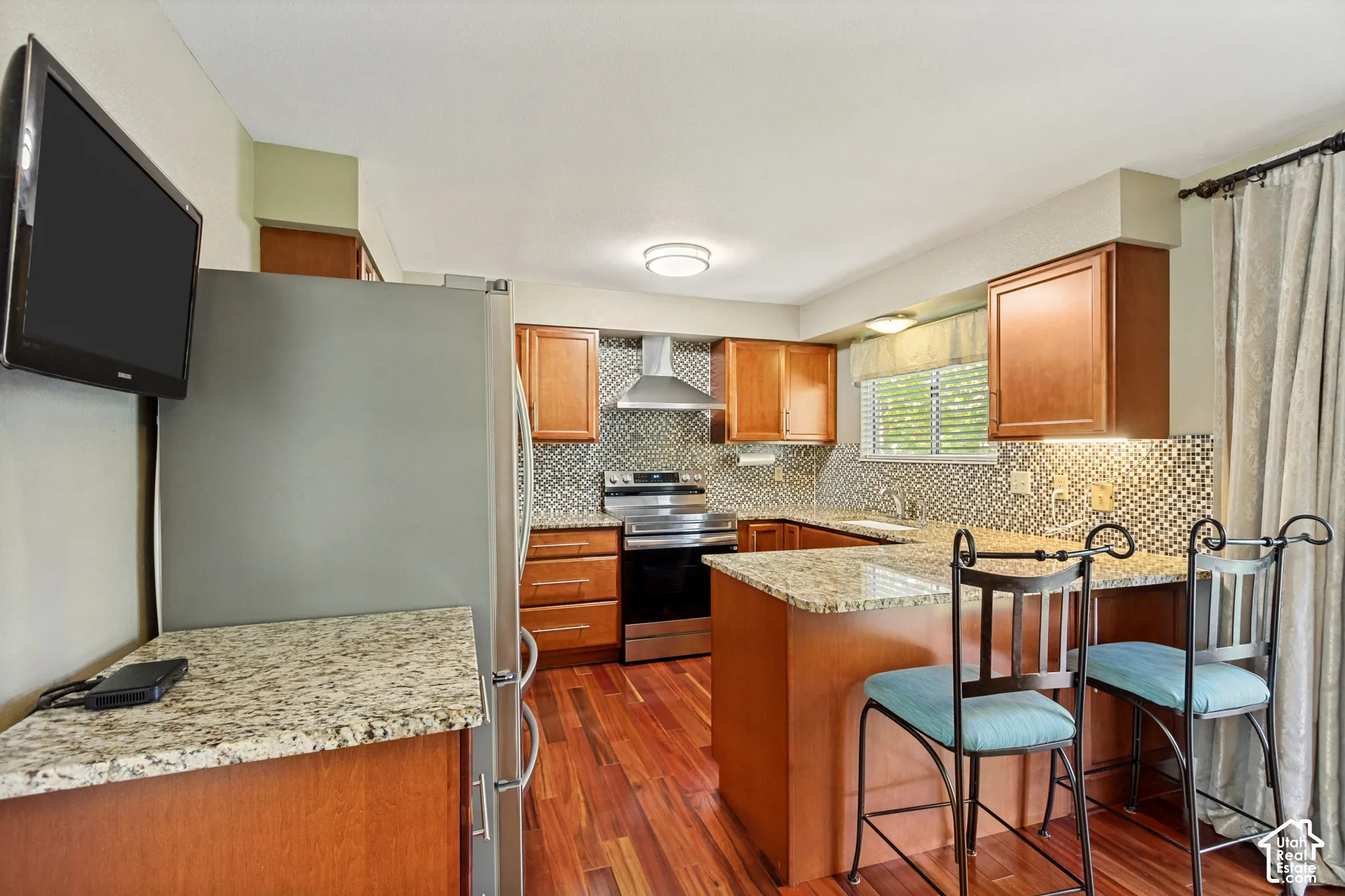 Kitchen featuring wood cabinetry, stone-finish countertops, stainless steel appliances, a tile backsplash, and wood-finish flooring