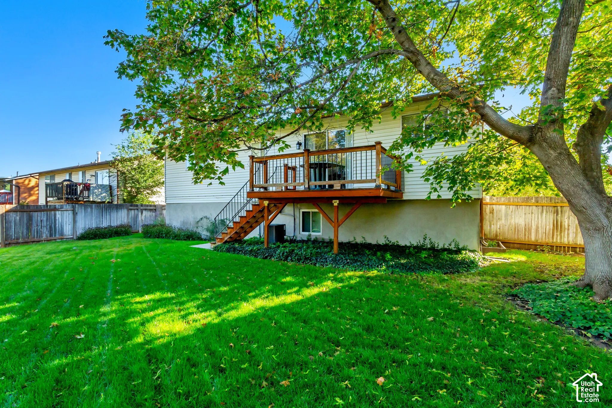 Elevated wood deck featuring metal balusters, stairs, and mature trees situated within a grass lawn enclosed by wooden fencing