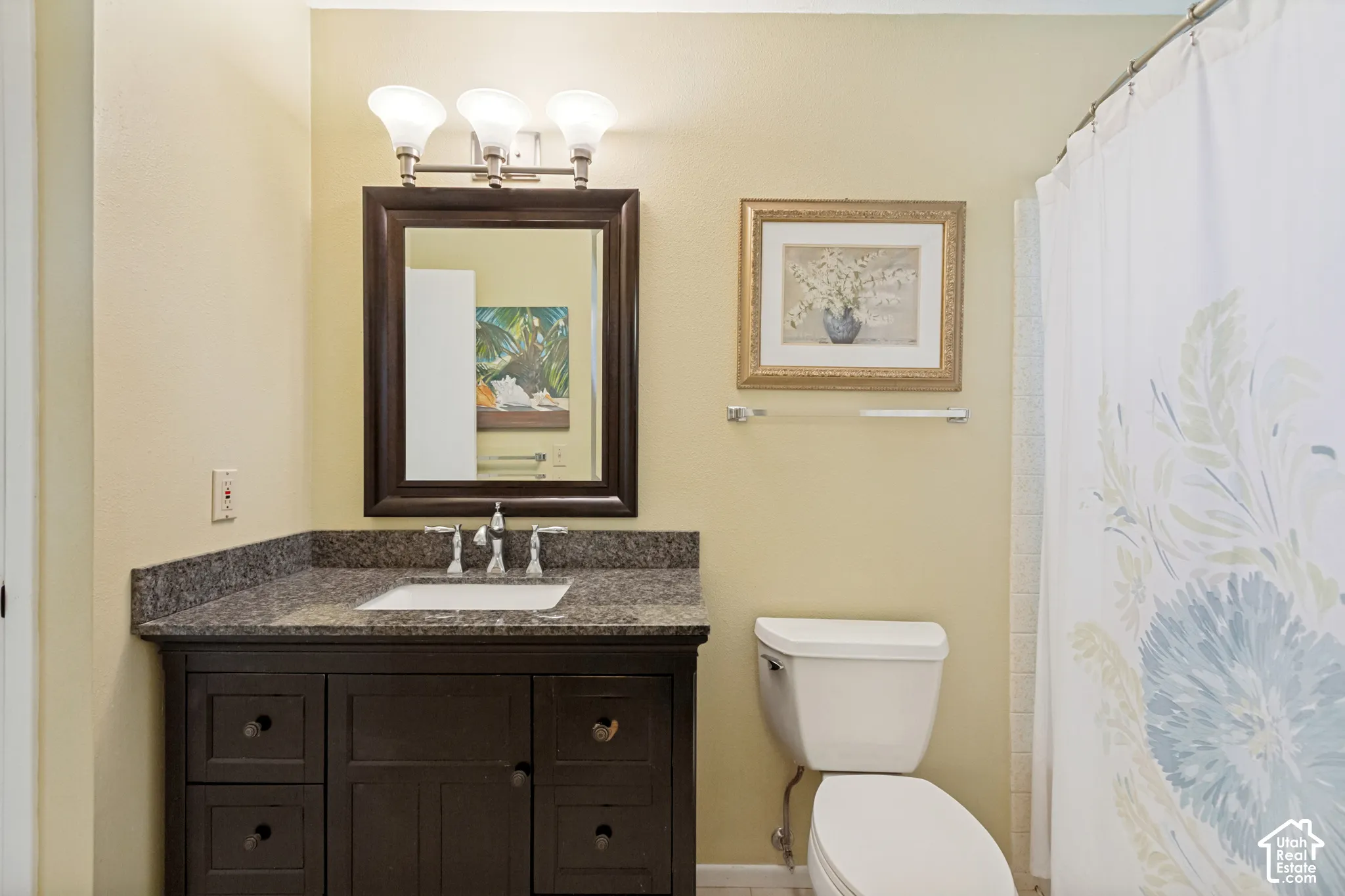 Dark wood vanity featuring a stone countertop, integrated undermount sink, three-light vanity fixture, and rectangular framed mirror