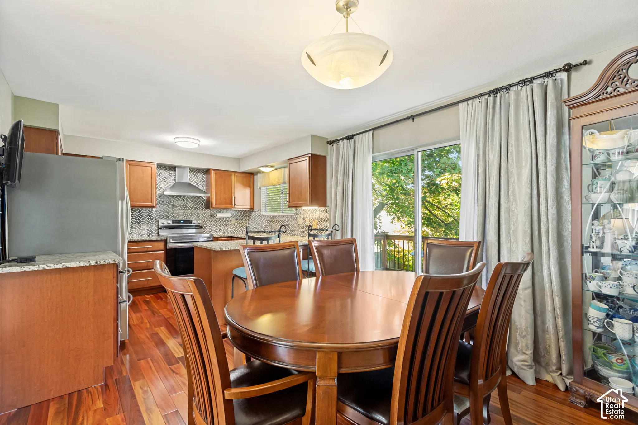 Kitchen featuring wood cabinetry, stone countertops, a mosaic tile backsplash, stainless steel range hood, and wood-finish flooring with sliding glass door access to an exterior deck