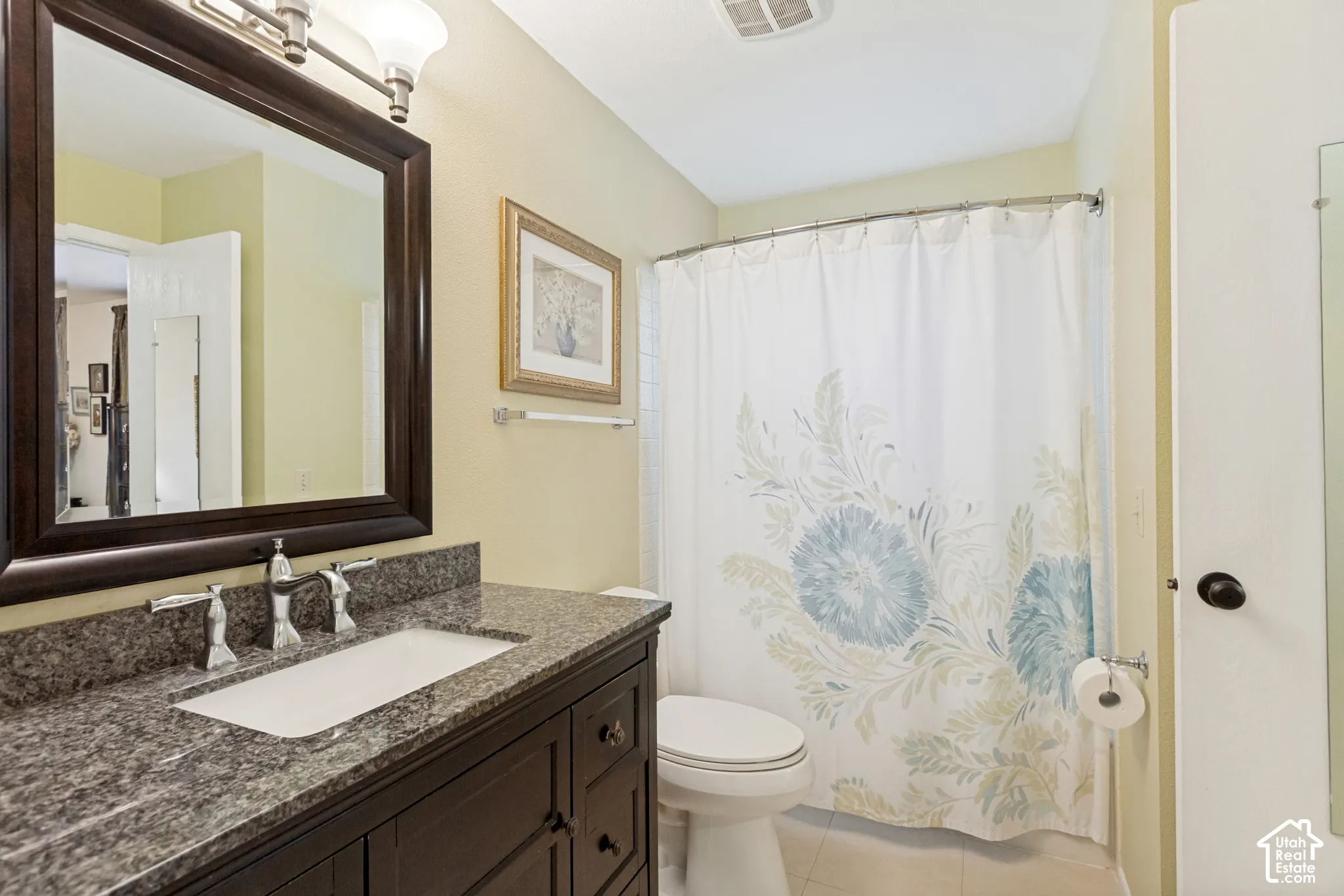 Bathroom vanity featuring a stone countertop, an integrated rectangular sink, dark wood-finish cabinetry, a framed wall mirror, and chrome finish hardware